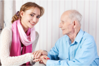 A caregiver smiling while hodling the hand of her patient